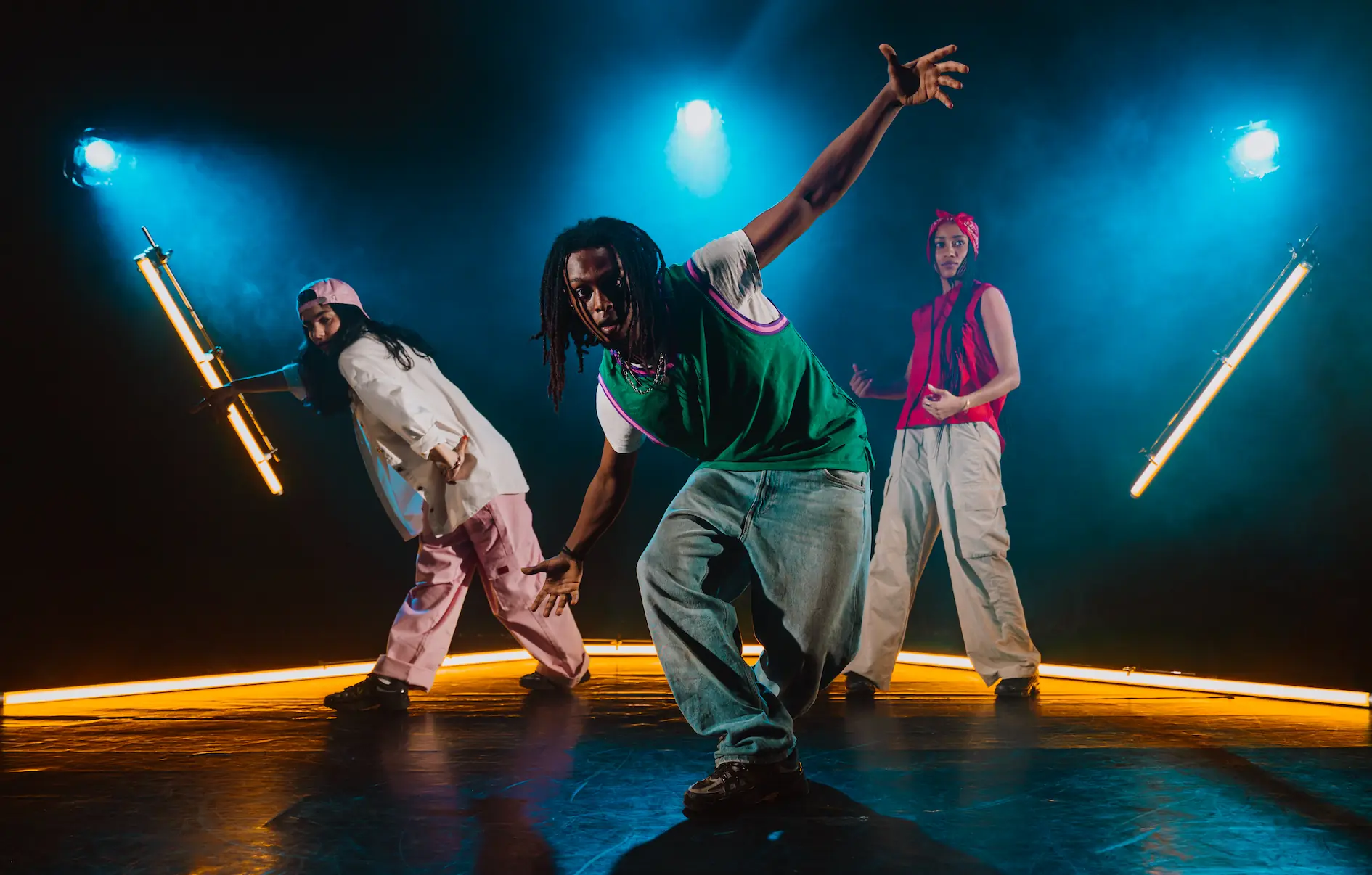Three dancers performing together under blue stage lights